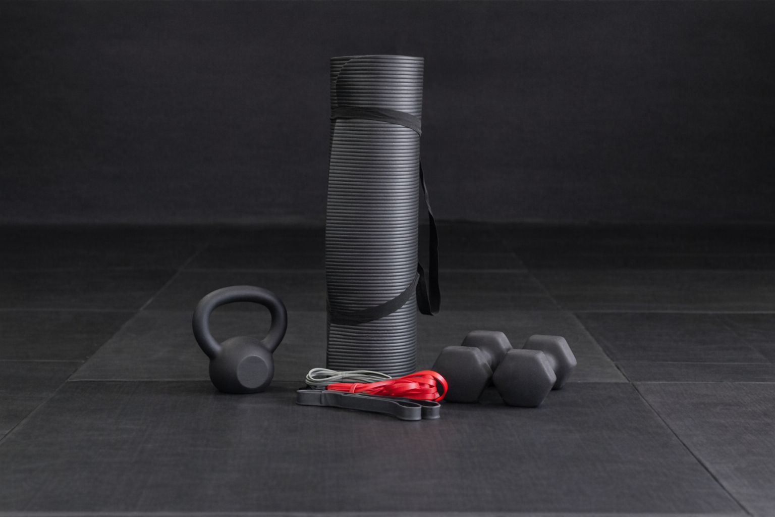 Träningsutrustning för hemmagym, med hantlar, kettlebell och yogamatta på golv.