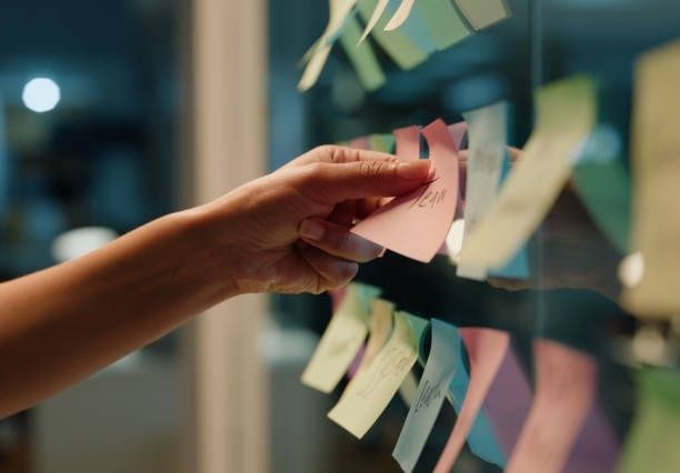 Hand organiserar färgglada post-it-lappar på en glasvägg